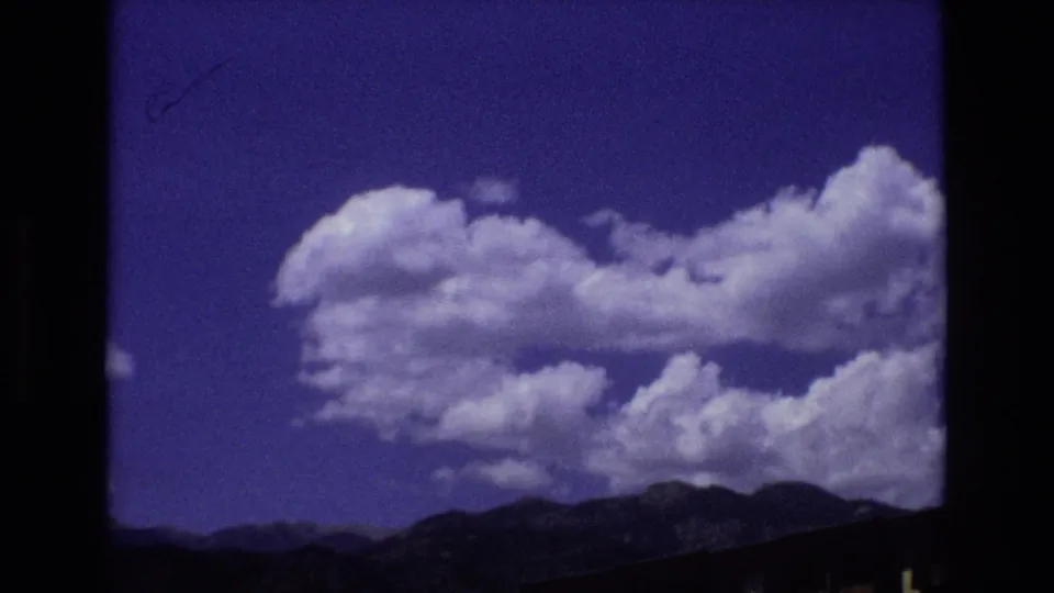 Colorado mountain landscape with a large white cumulus cloud crossing a deep blue sky above dark ridgelines in 1973 home-movie footage.