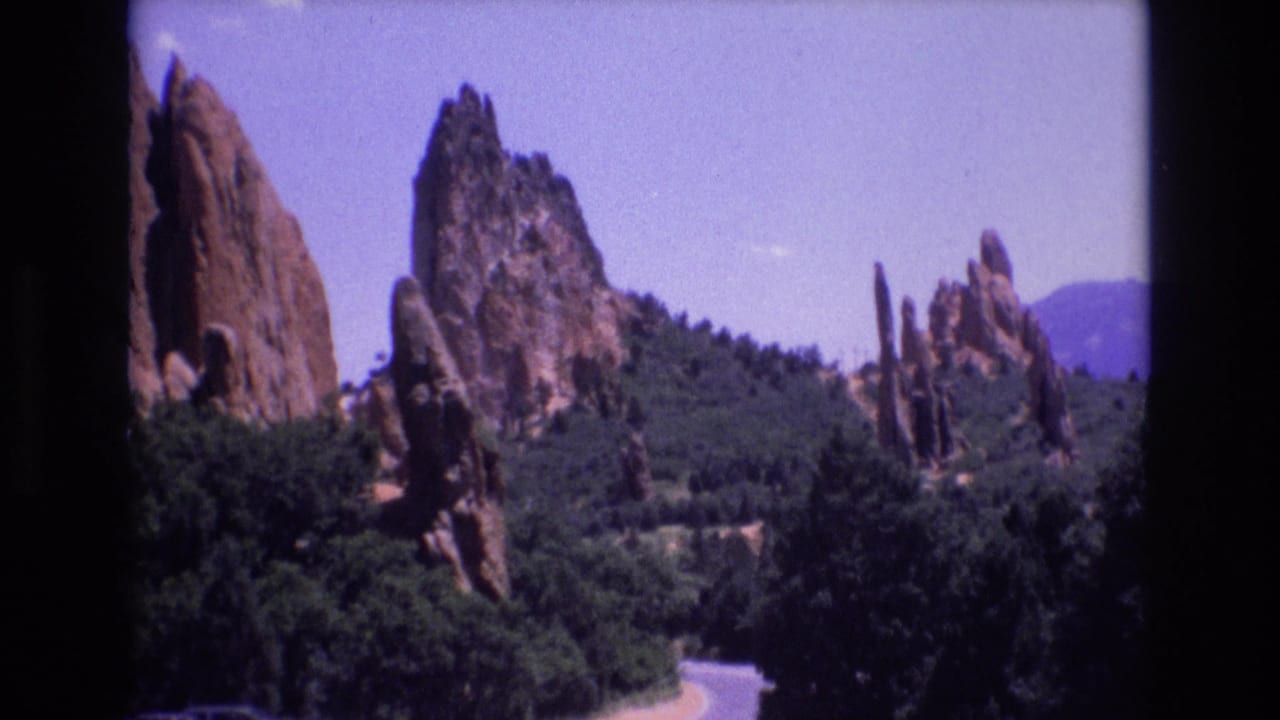 Red rock spires and green trees above a curving road under a bright sky.