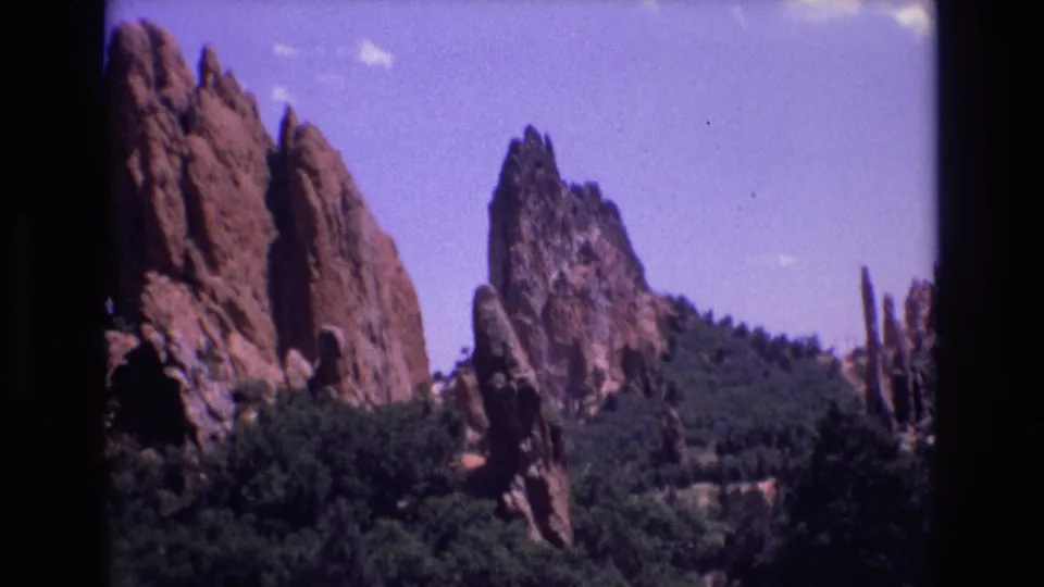 1973 Colorado 8mm frame with large red sandstone slabs, dense green trees, and smaller vertical rock formations beyond.