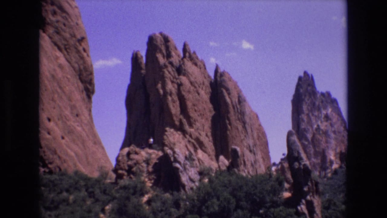 Tall red rock fins stand behind shrubs beneath a clear blue sky.