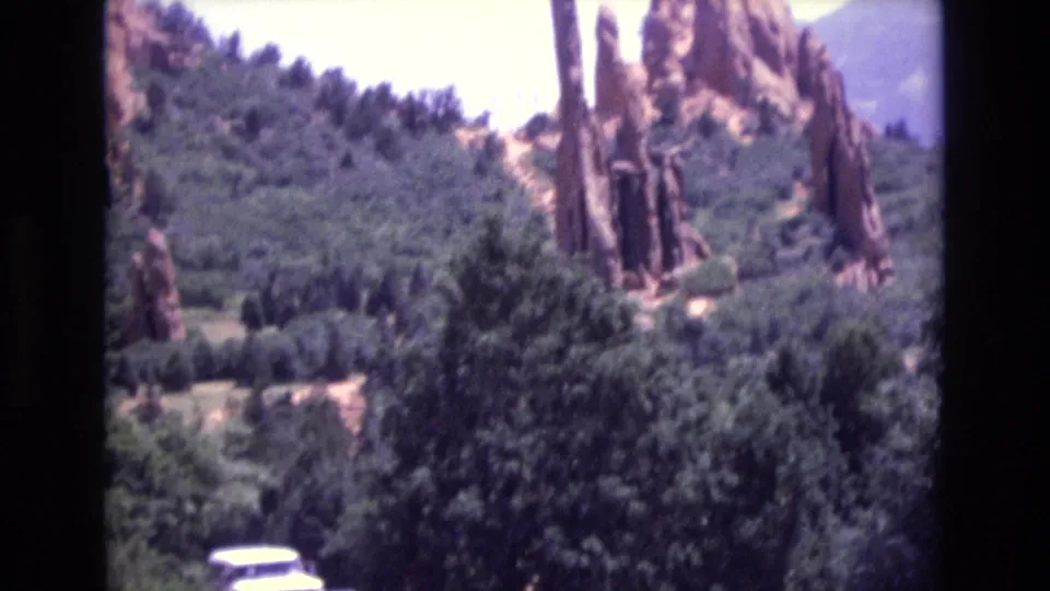 1973 Colorado frame with red sandstone spires, wooded foreground, distant hills, and the roof of a car partly visible near the road.