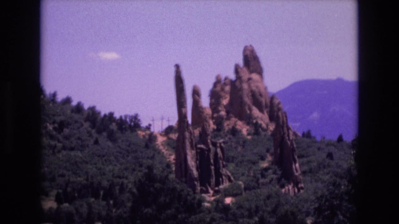1973 8mm home-movie view of Garden of the Gods in Colorado, showing red sandstone formations, green foothills, and distant mountains.