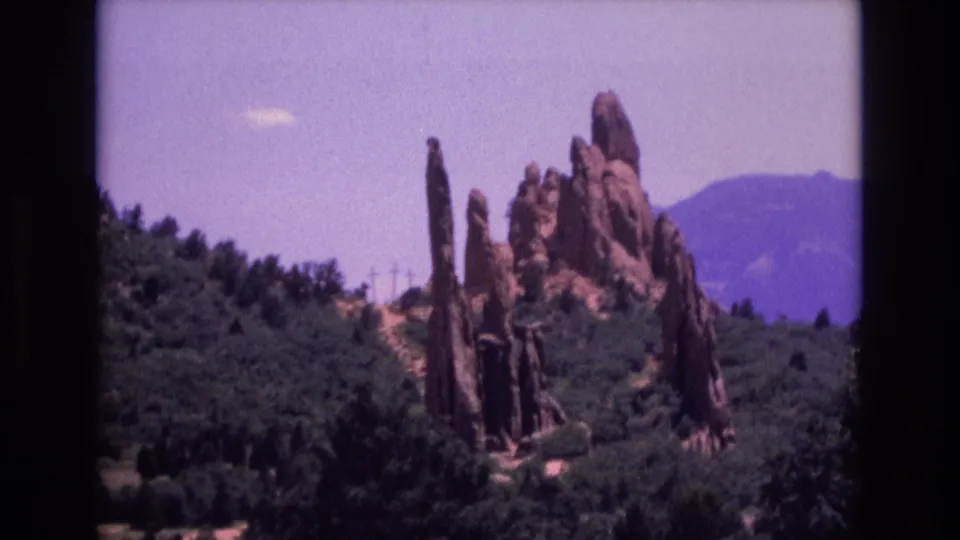 Garden of the Gods sandstone formations in Colorado appear beyond a wooded slope in this 1973 visitor-shot 8mm frame.