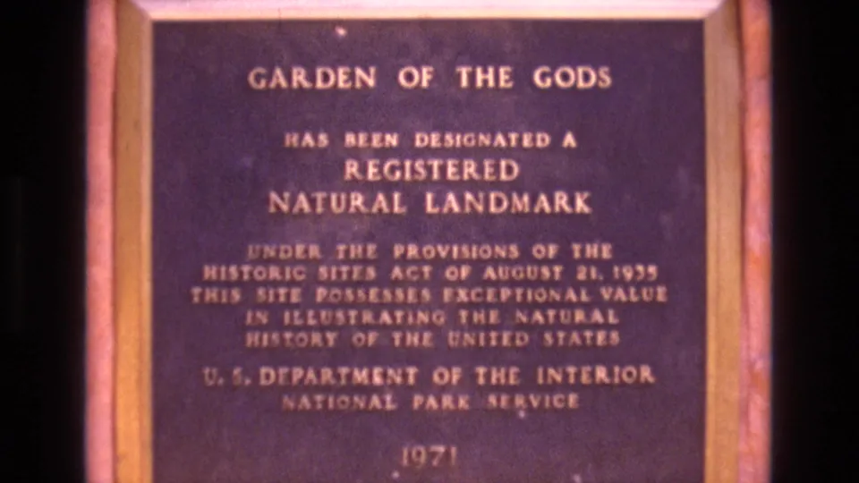 1973 Colorado home-movie frame showing the Garden of the Gods Registered Natural Landmark plaque with soft focus, warm color shift, and a reddish border around the sign.