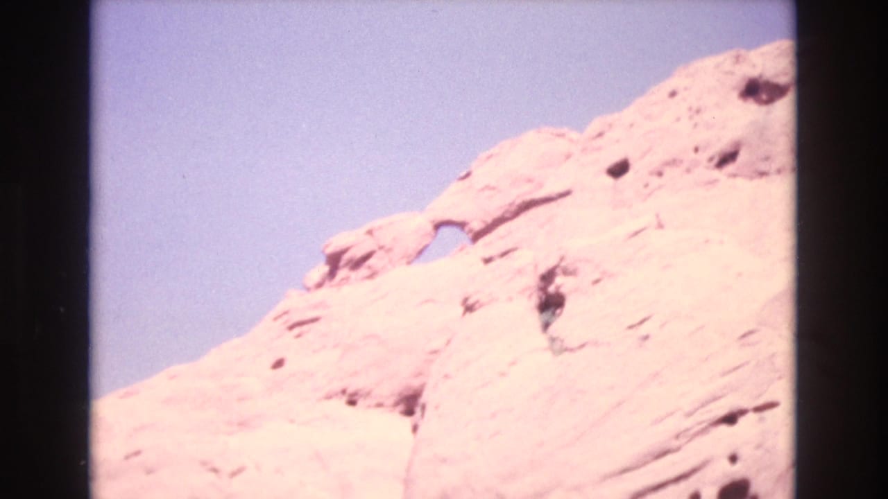 Sunlit pale sandstone rock formation with a small natural arch under blue sky.