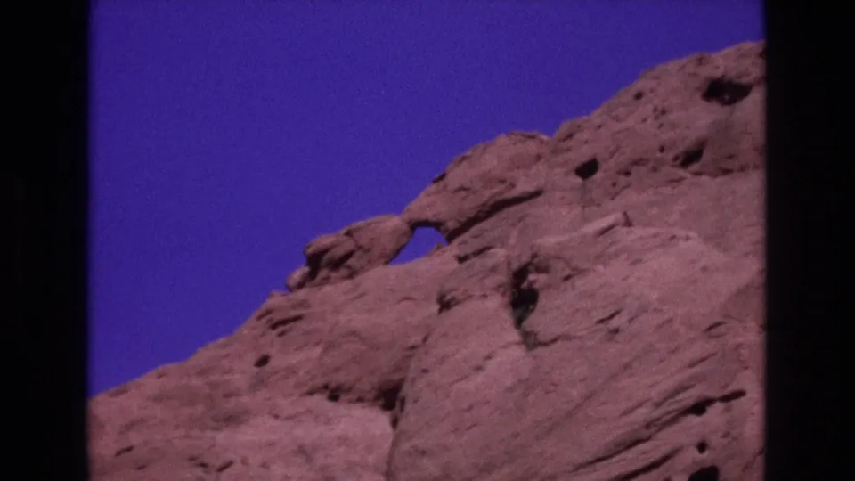 1973 Colorado 8mm frame showing a pinkish sandstone rock face, erosion holes, and a small natural arch at Garden of the Gods.