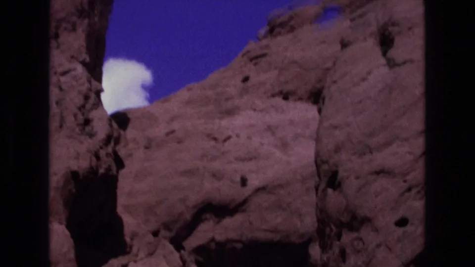 1973 Colorado home-movie frame of rugged sandstone formations with a white cloud seen near an eroded cutout.