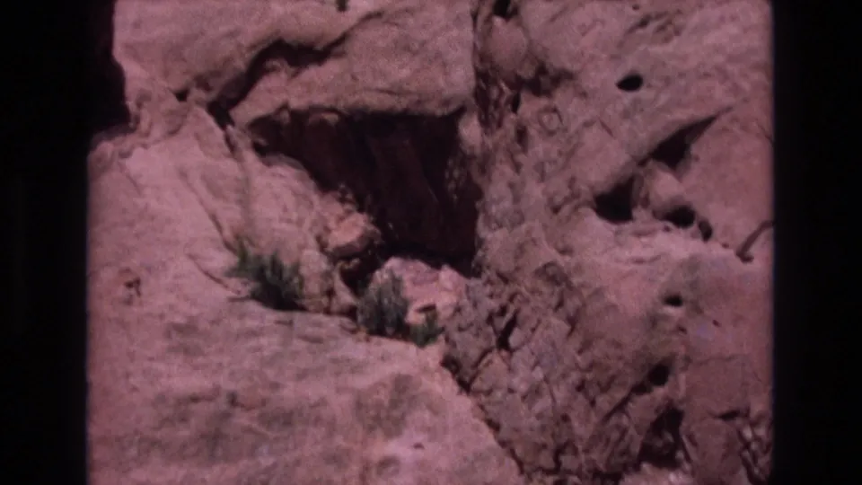 1973 Colorado 8mm frame showing a closer view of eroded reddish rock and small desert vegetation in a canyon setting.