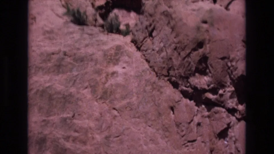 1973 Colorado home-movie frame of rugged reddish sandstone, cracks, and sparse vegetation during a handheld canyon pan.
