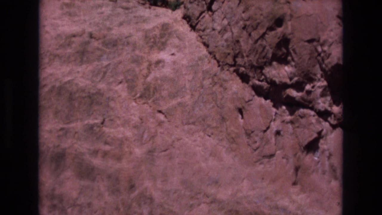 1973 Colorado 8mm frame showing a close-up of a reddish-brown rock surface with cracks, raised rough areas, and dark film borders.