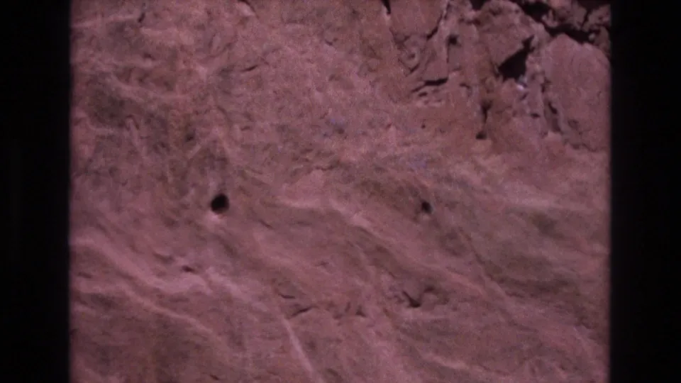 1973 Colorado 8mm frame showing reddish stone with pale erosion-like streaks, small dark pits, and a vertical black film-frame edge.