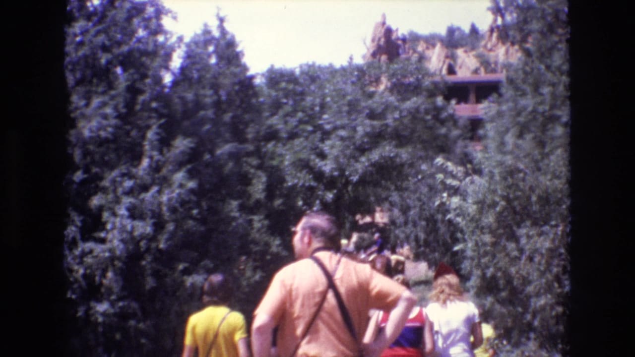 Visitors stand and walk under trees near hillside tipi-like structures.