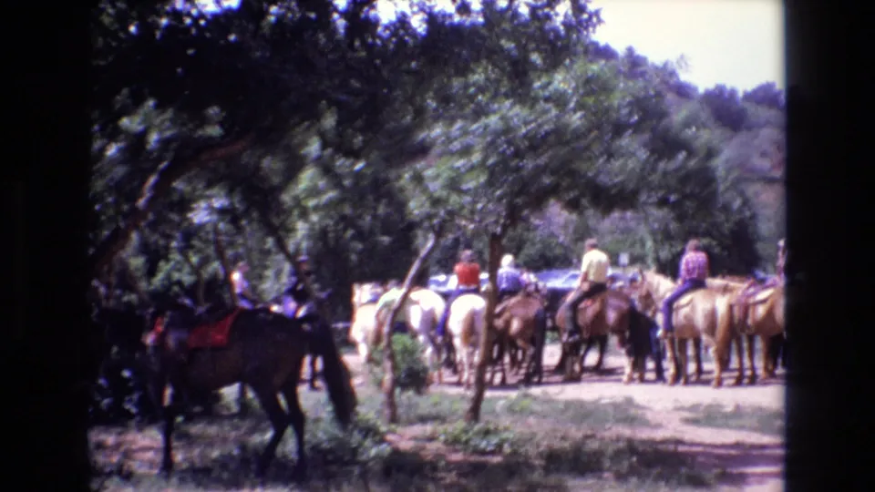 Horses and riders wait in a shaded outdoor riding area, with tourists and tree cover visible in the Colorado 8mm travel footage.