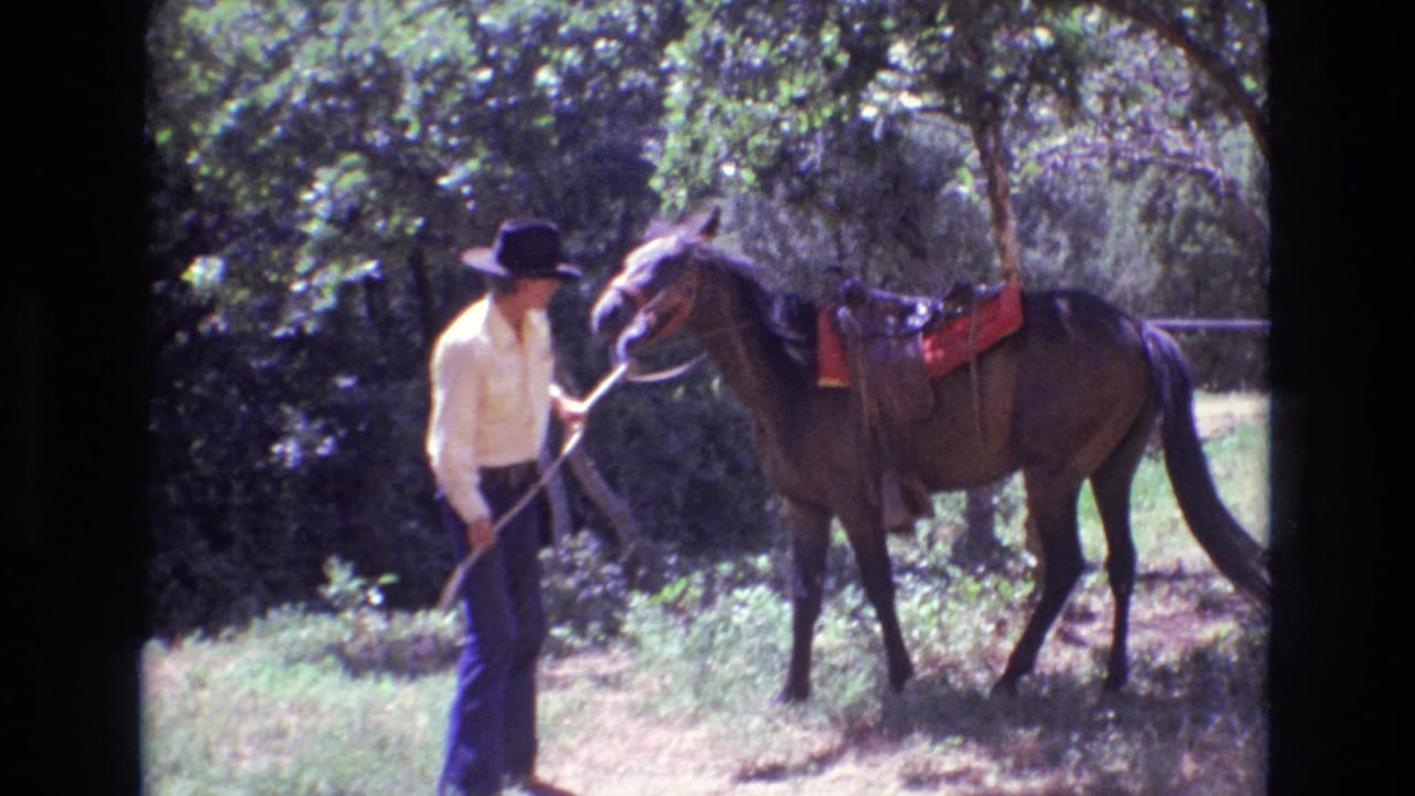 Man holding reins beside a saddled horse with a red saddle blanket.