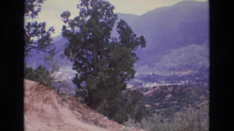 1973 Colorado 8mm frame looking past trees and a sandy foreground toward a broad valley and distant mountains.
