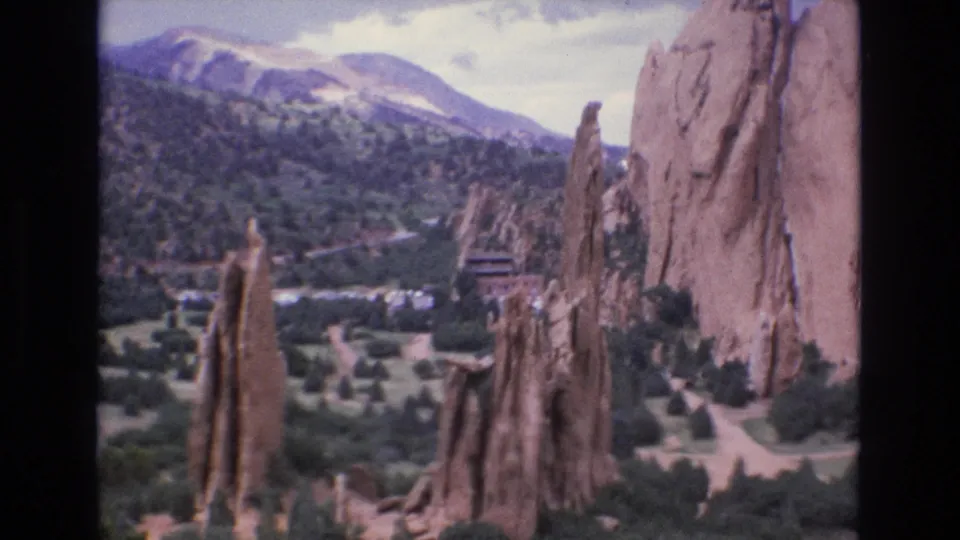 1973 Colorado home-movie view of Garden of the Gods red sandstone spires, green parkland, paths, and mountains beyond.