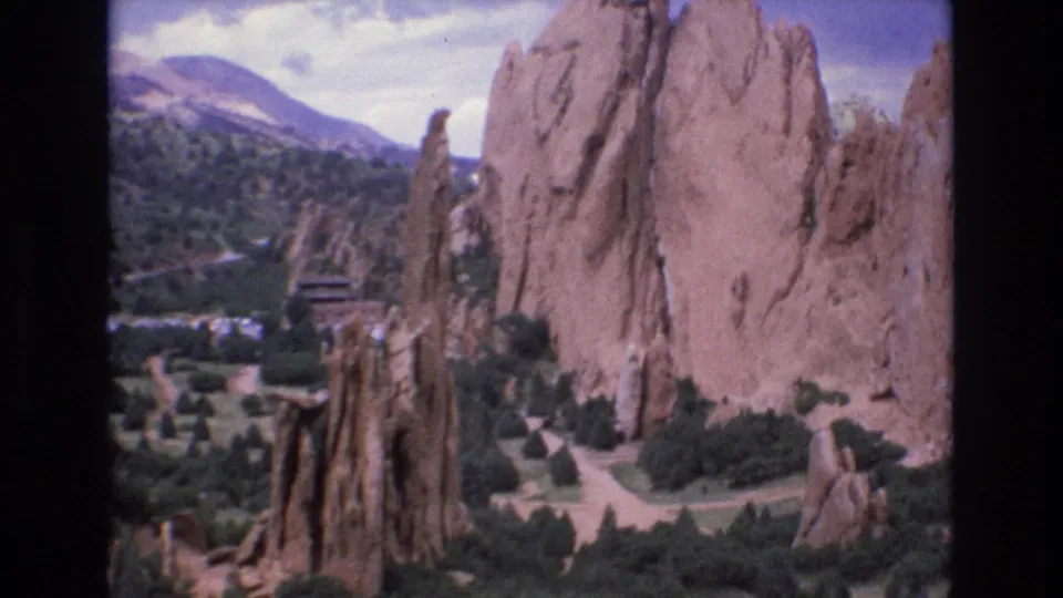 1973 Colorado 8mm frame showing tall Garden of the Gods sandstone formations, low shrubs, park paths, and mountains in the background.