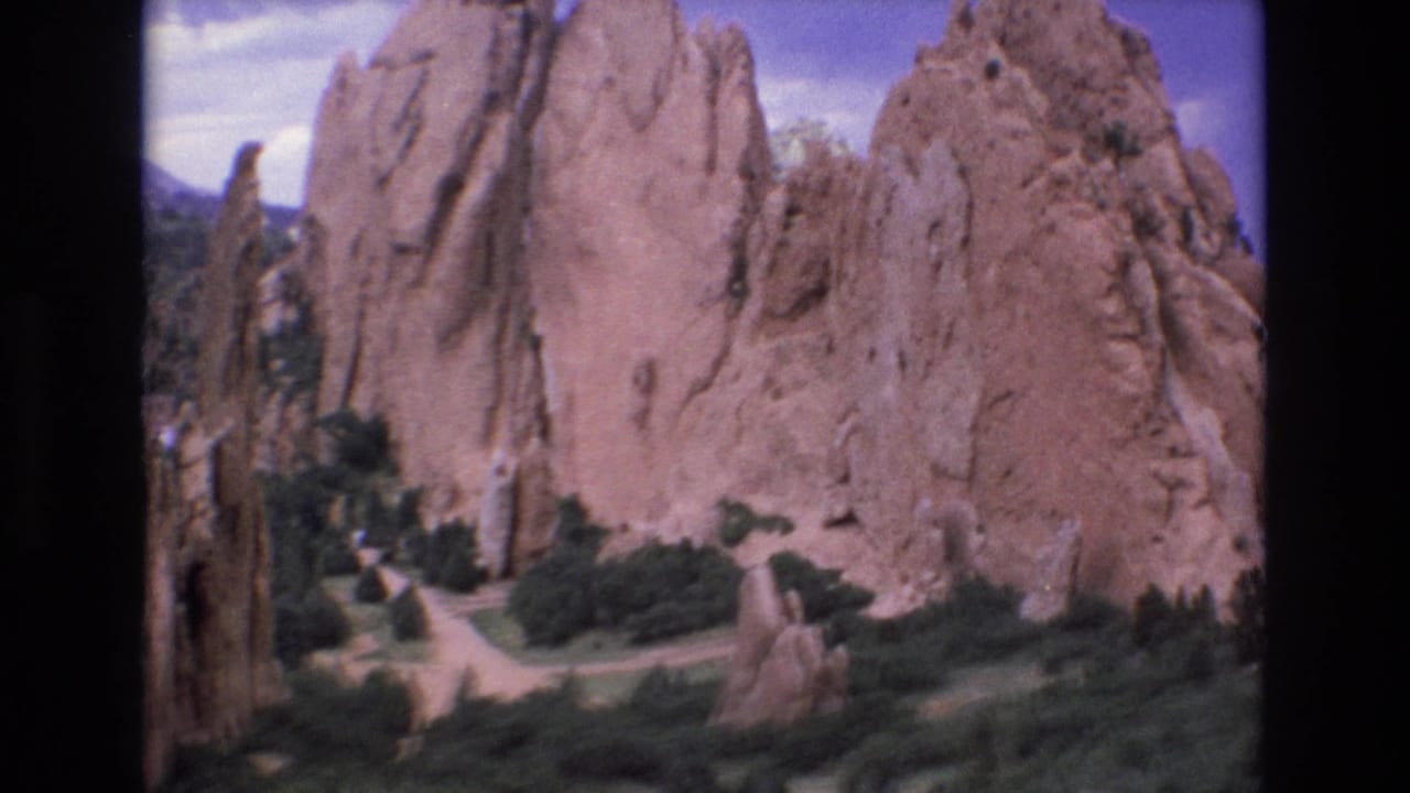 1973 Colorado 8mm frame showing Garden of the Gods sandstone spires rising above green shrubs and winding paths under a blue sky.