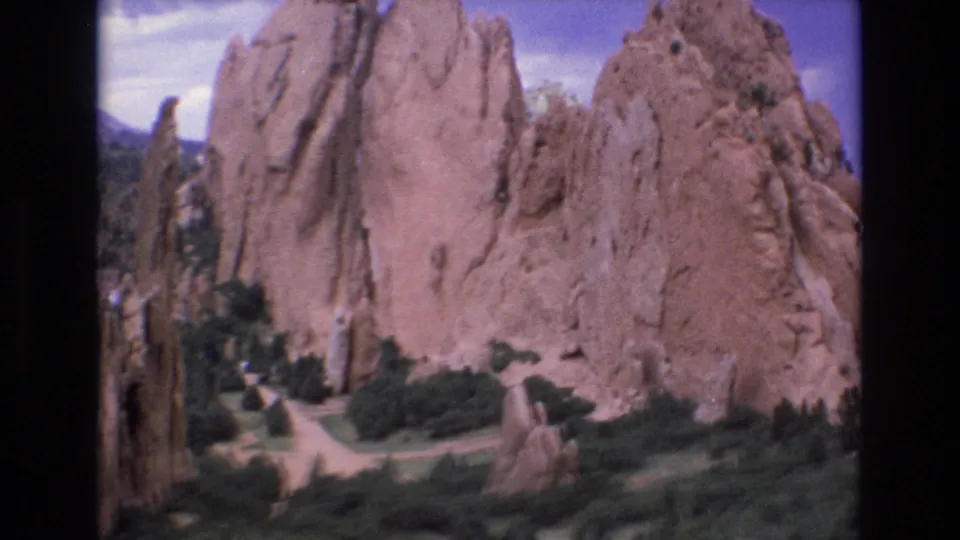1973 Colorado 8mm frame showing Garden of the Gods sandstone spires rising above green shrubs and winding paths under a blue sky.