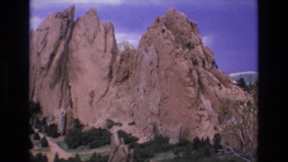 1973 Colorado 8mm frame with Garden of the Gods rock fins, low shrubs, scattered trees, and a bright blue sky in a handheld scenic view.