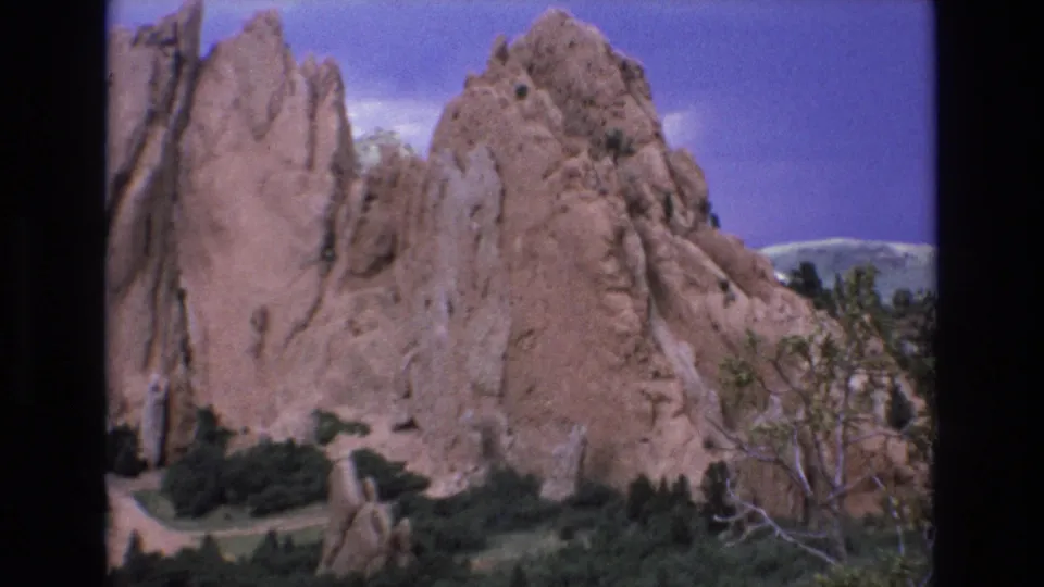 1973 Colorado 8mm frame showing a closer visitor view of Garden of the Gods sandstone walls with brush, trees, and distant hills beyond.