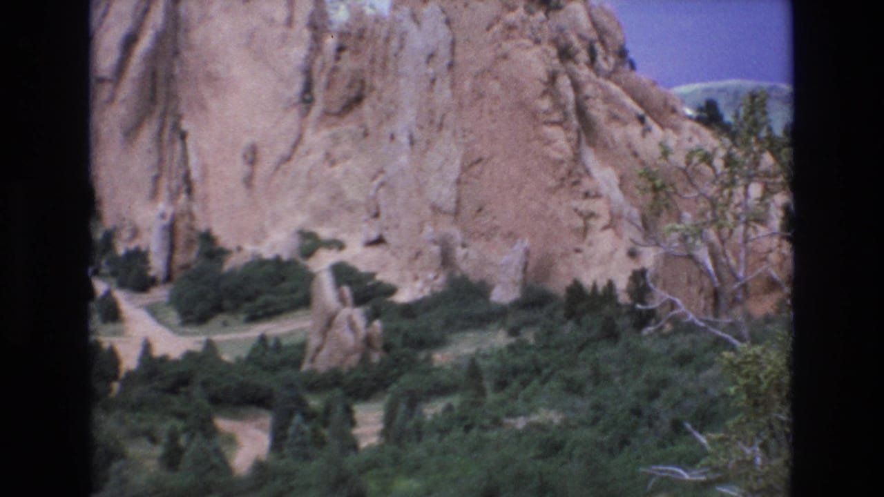 1973 Colorado 8mm frame showing red sandstone walls, a freestanding rock form, dark green vegetation, and pale winding park paths.