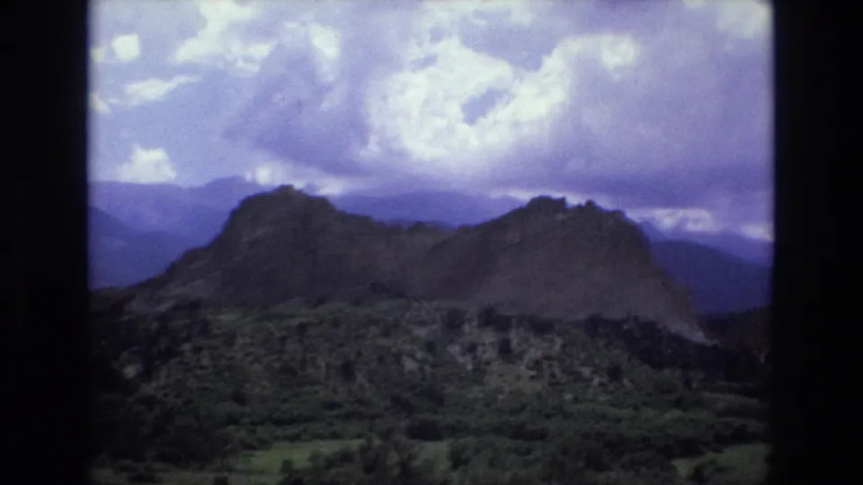 1973 Colorado 8mm frame looking across a forested valley toward a dark mountain ridge under a cloudy purple-blue sky.