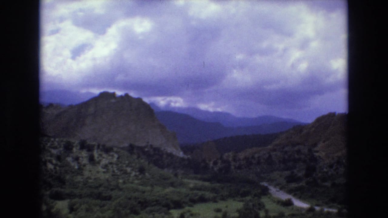 Mountain canyon landscape with a winding road under a cloudy sky.
