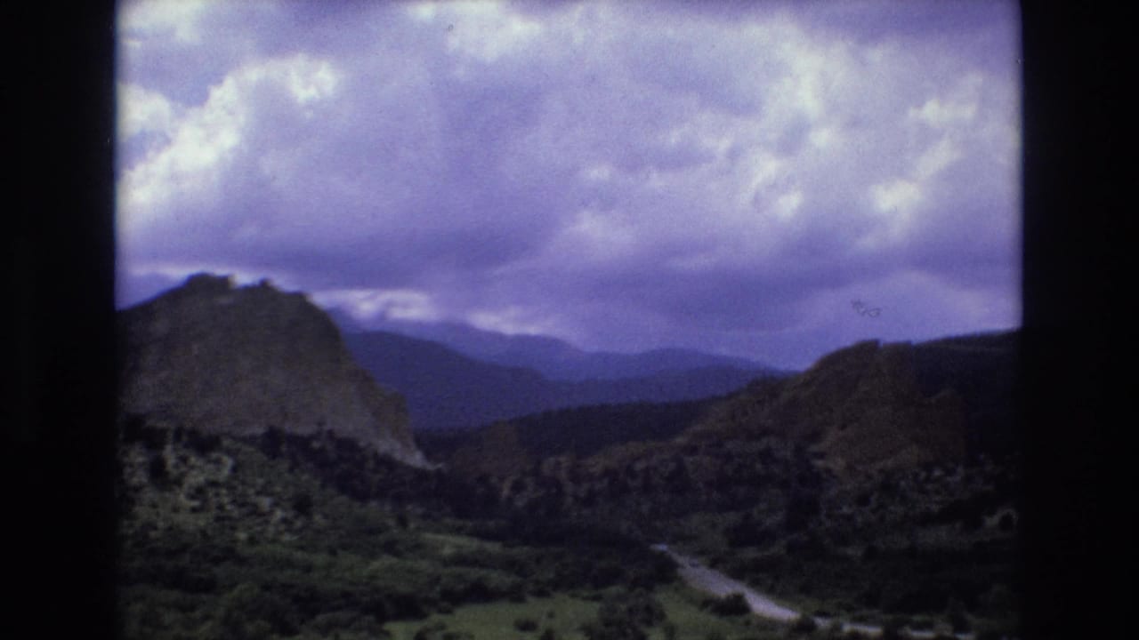 Wide canyon view with mountain ridges, vegetation, and overcast sky.