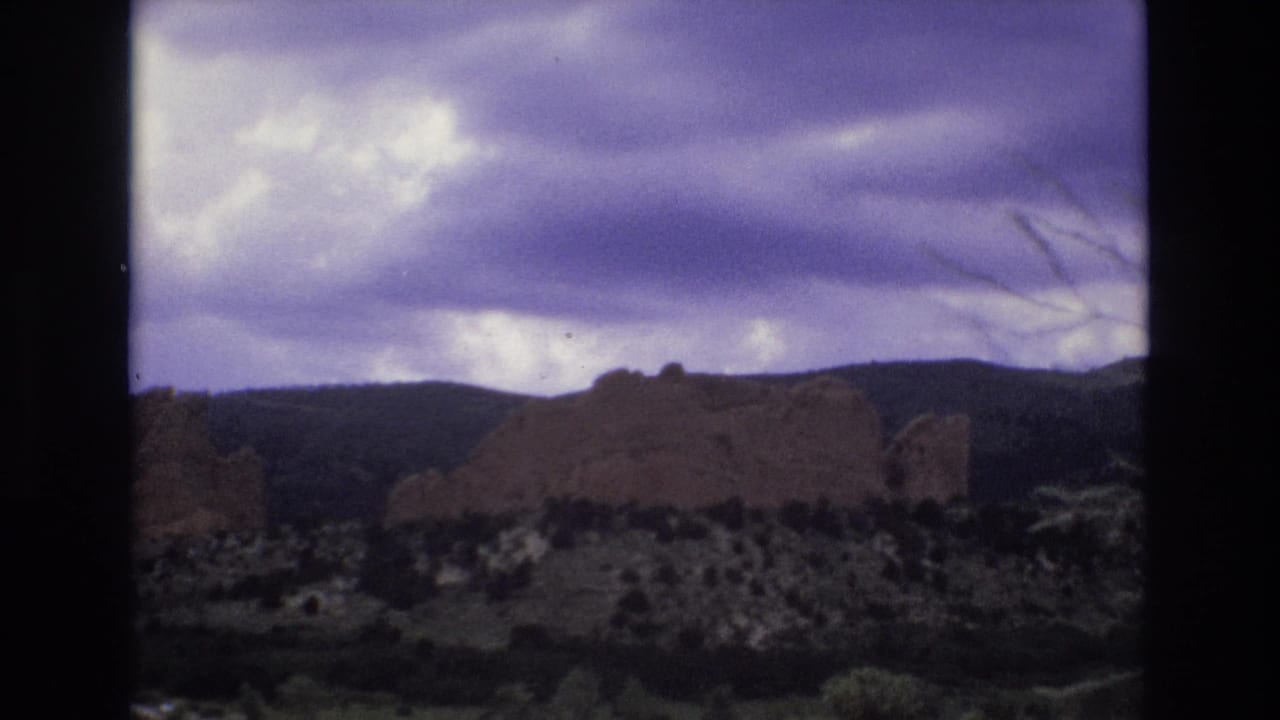 Red rock formations and distant hills beneath a cloudy sky.