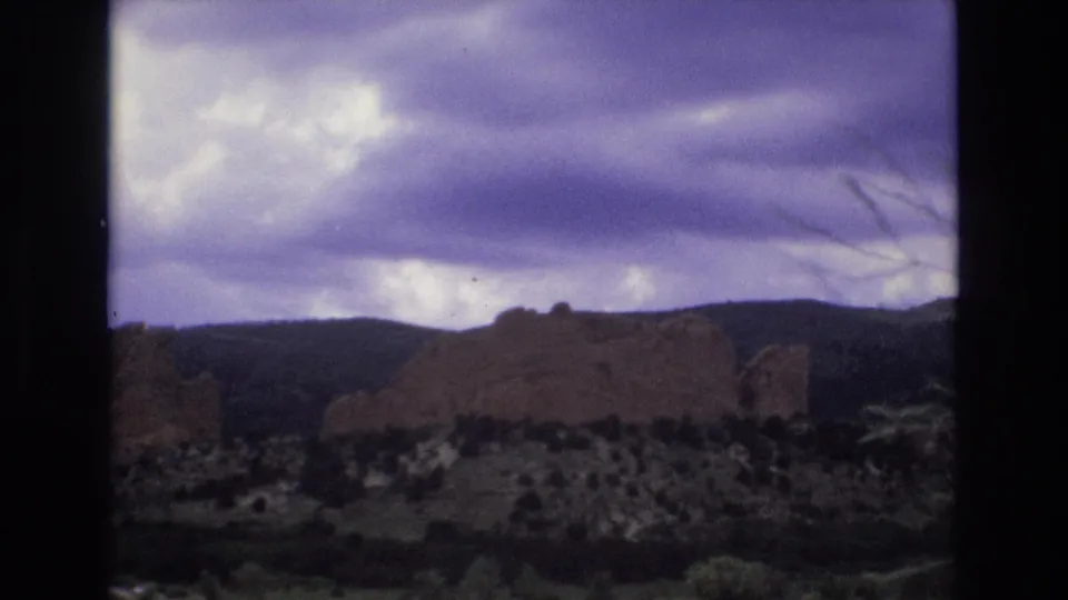A second view of Colorado red rock formations and low hills under a purple-blue cloudy sky, matching the supplied Garden of the Gods road-trip context.