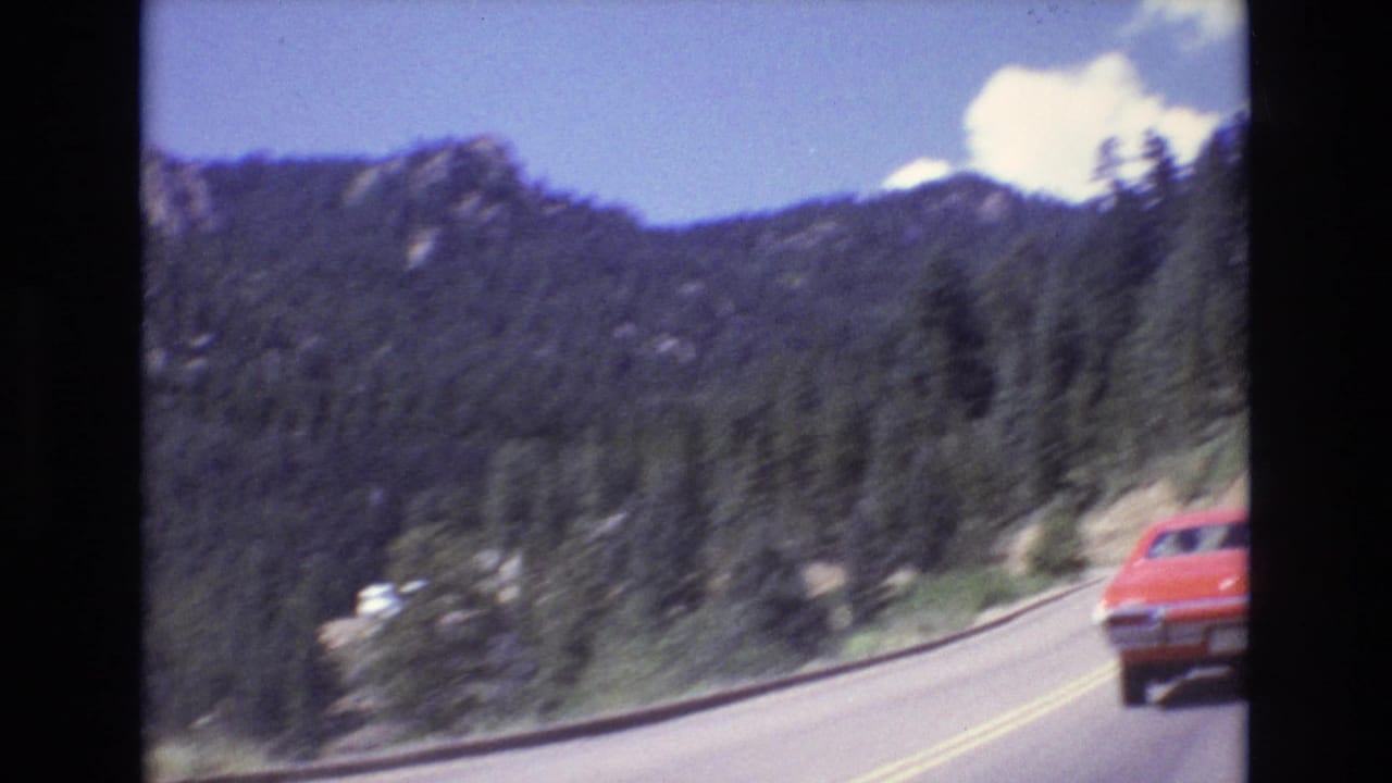 Red car driving on a mountain highway bordered by forested slopes.