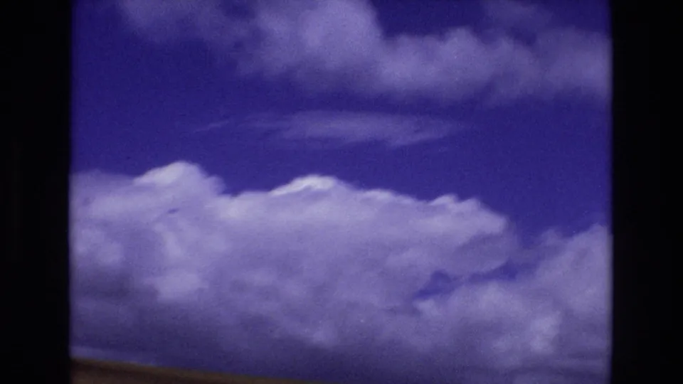 1973 Colorado 8mm frame focused on blue sky and large clouds, with the scan showing strong purple-blue color shift and soft film texture.