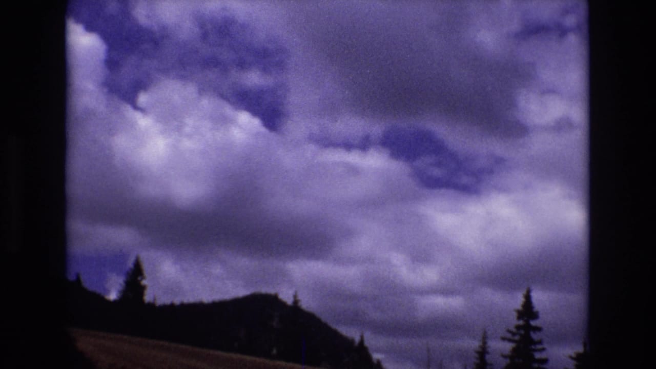 1973 Colorado 8mm frame showing purple-tinged clouds over a dark mountain ridge and evergreen silhouettes.