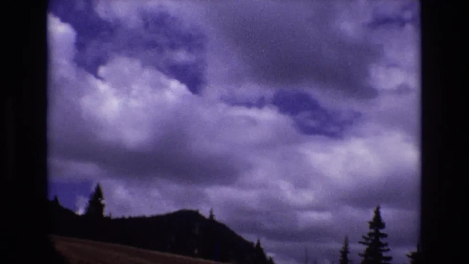 1973 Colorado 8mm frame showing purple-tinged clouds over a dark mountain ridge and evergreen silhouettes.