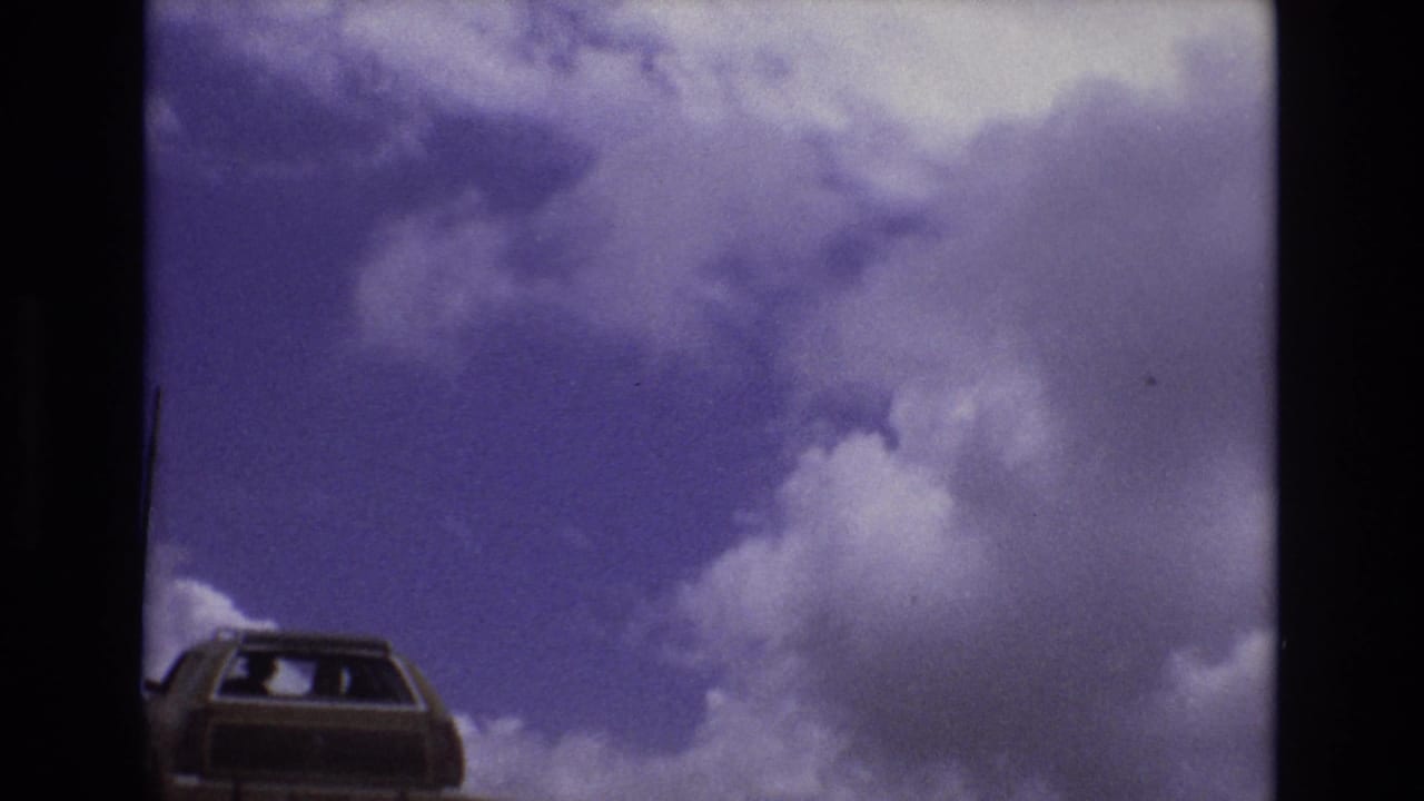 Station wagon low in frame beneath a purple-blue sky with large white clouds.
