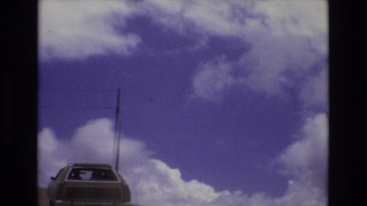 Station wagon on the road with a utility pole rising against a clouded sky.