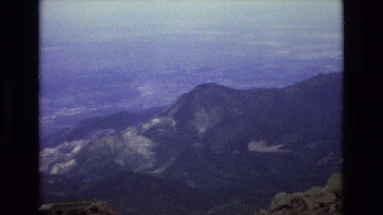 1973 Colorado 8mm frame showing layered mountain ridges and distant valleys from a high alpine viewpoint under a hazy sky.