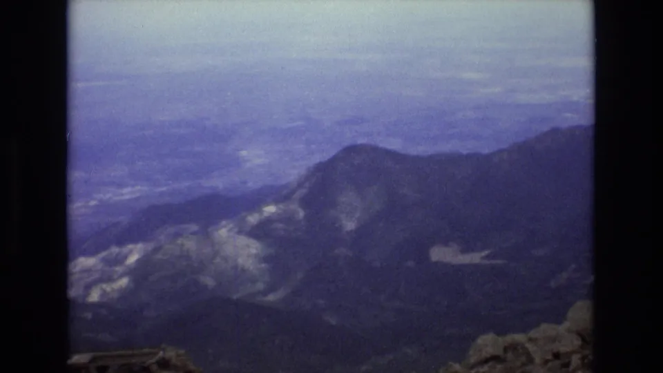 1973 Colorado 8mm frame showing layered mountain ridges and distant valleys from a high alpine viewpoint under a hazy sky.