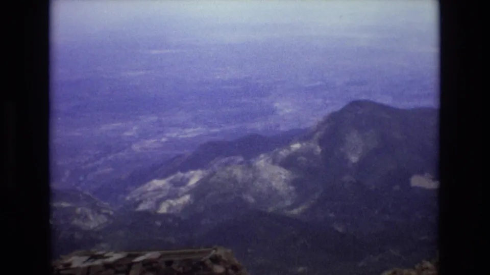 1973 Colorado home-movie frame with a rounded mountain peak, layered ridges, distant valley haze, and dark 8mm frame edges.