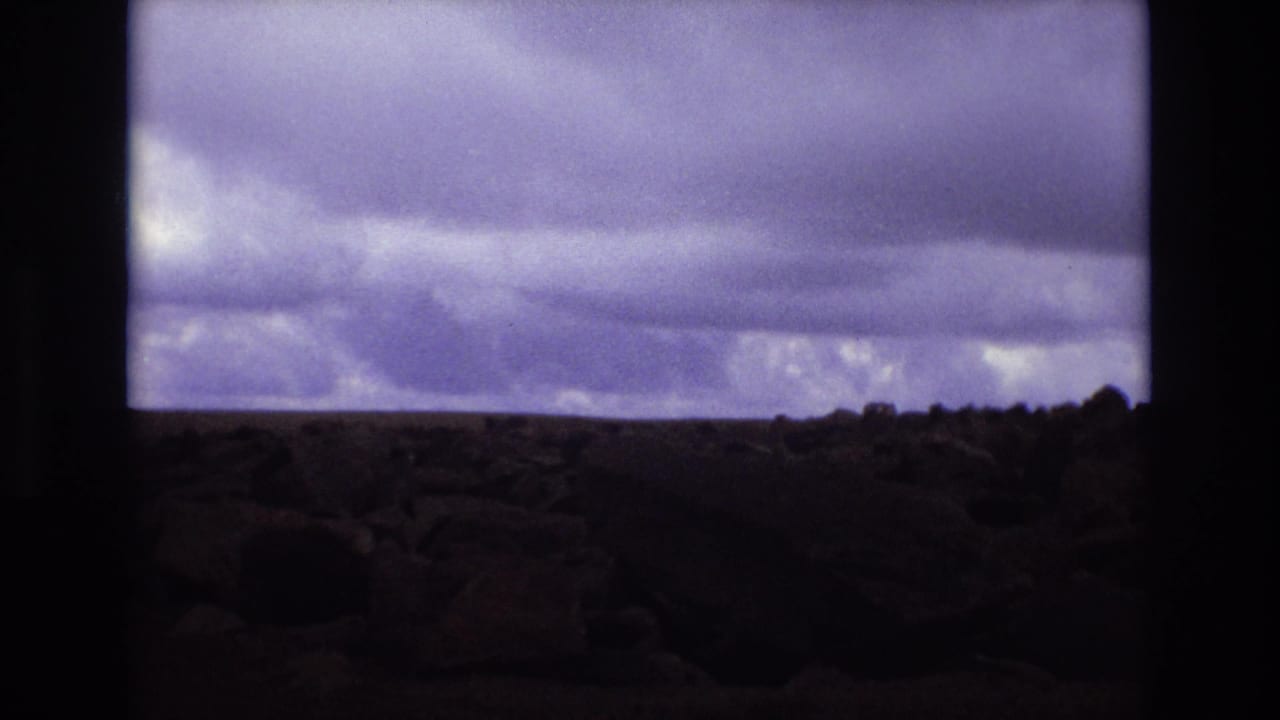 Colorado 1973 8mm frame showing a low rocky landscape under a broad band of dark pre-storm clouds.