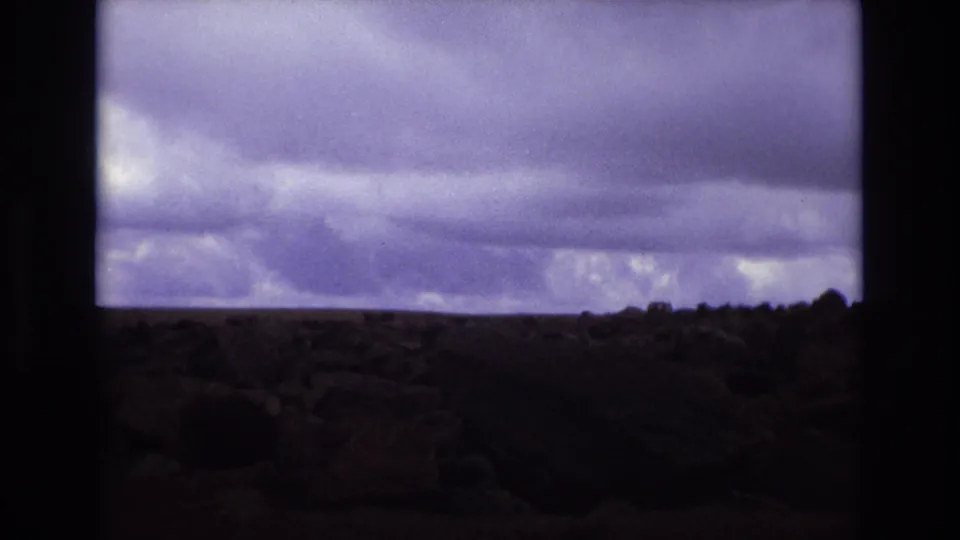 Colorado 1973 8mm frame showing a low rocky landscape under a broad band of dark pre-storm clouds.