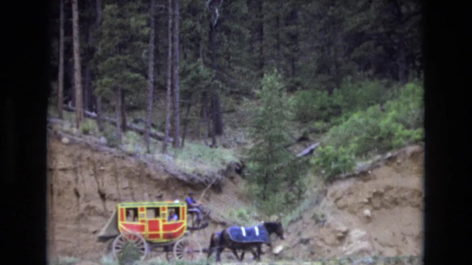 The carriage and horse pass through the lower edge of the frame, with brush, pine trees, and a steep dirt bank filling the Colorado mountain setting.