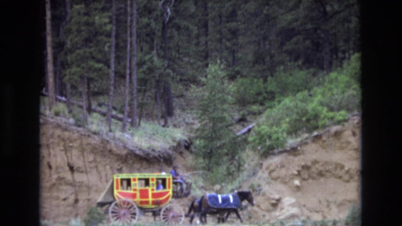 A red and yellow stagecoach-style carriage pulled by two horses moves along a dirt road in a forested Colorado mountain setting in 1973.