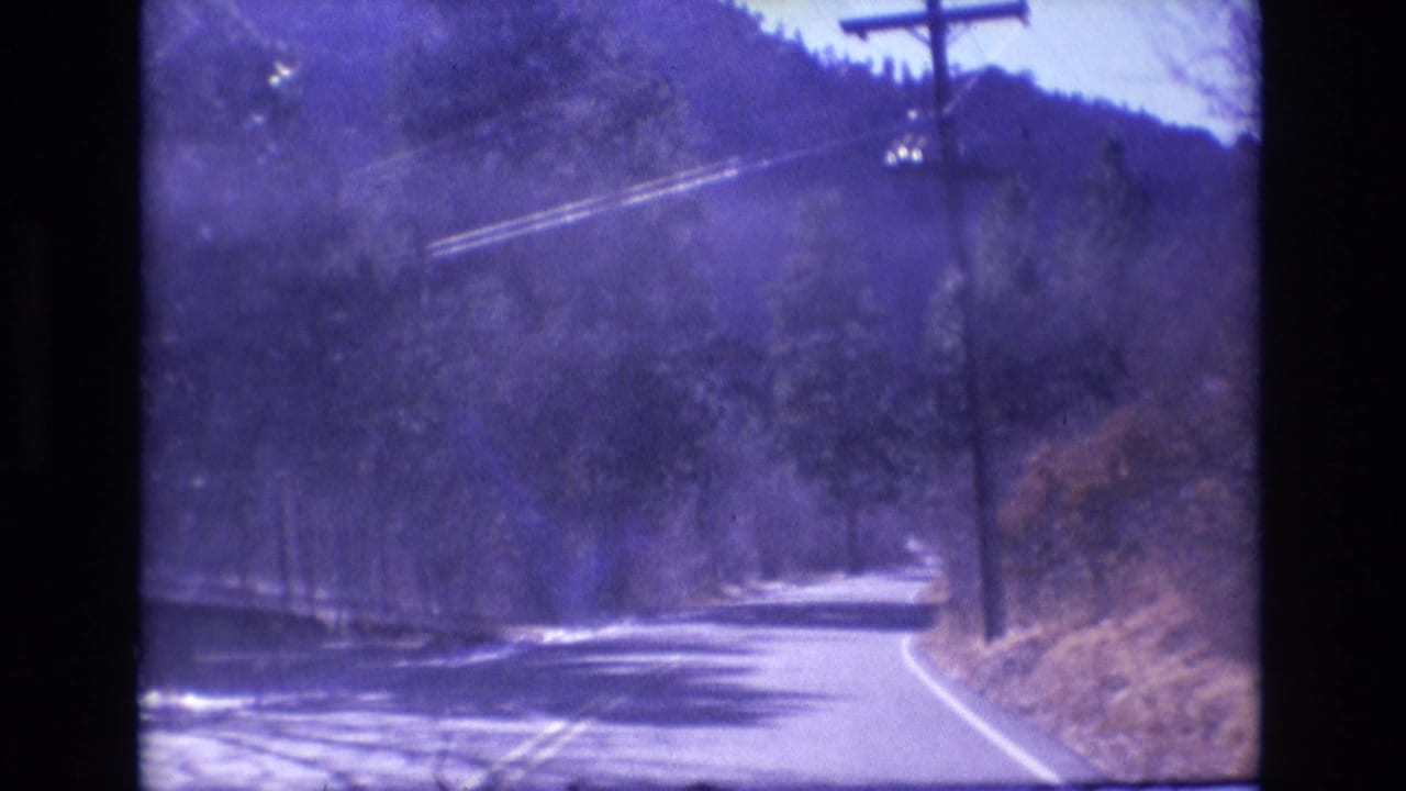 1973 Colorado 8mm frame showing a paved mountain road curving through trees with a utility pole and overhead power lines visible beside the route.
