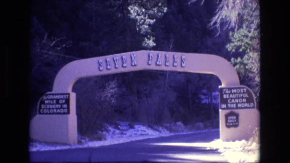The clip ends on the Seven Falls entrance arch in Colorado, with the road passing beneath it and readable tourist signage on the arch supports.