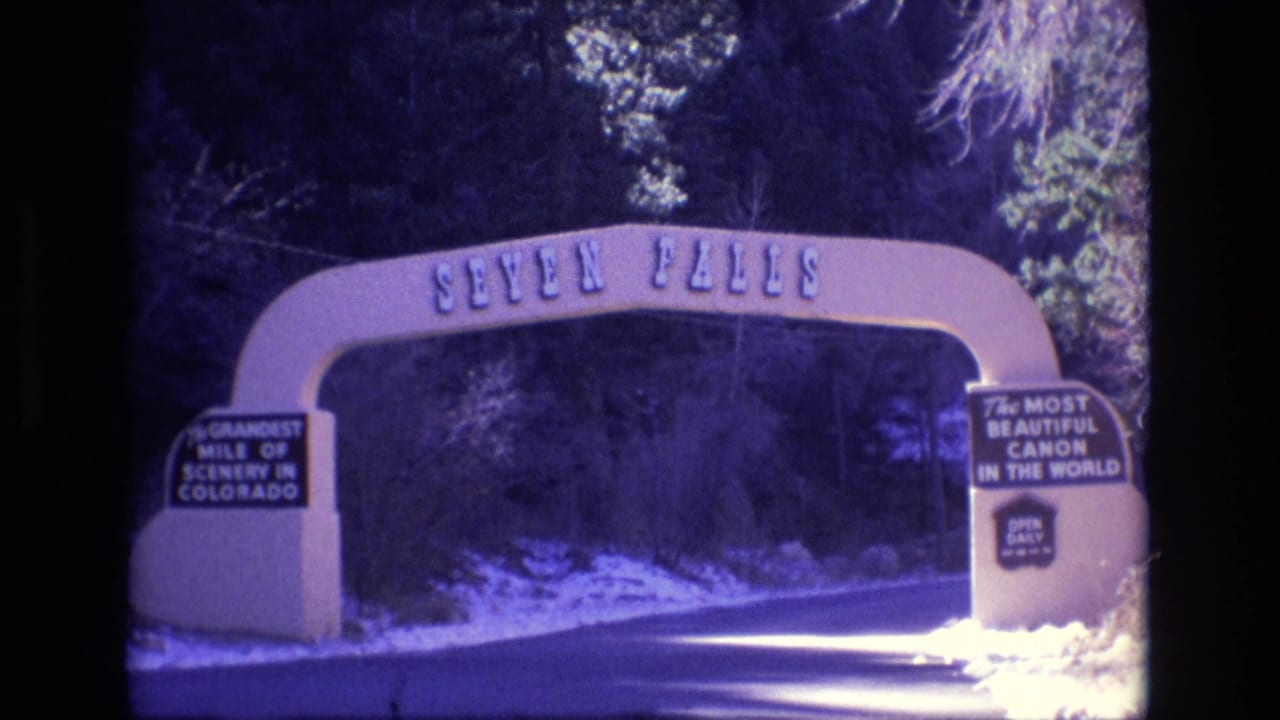 Seven Falls entrance arch over a road with snow and roadside signs.