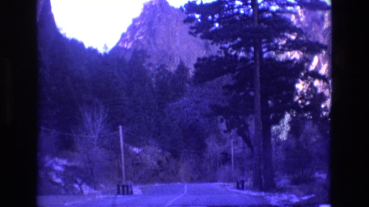 Forest road with utility poles beneath rugged mountain peaks.