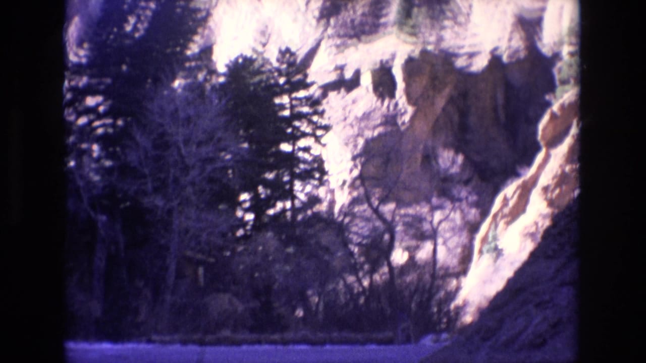 Rocky mountain slope with trees beside a road edge.