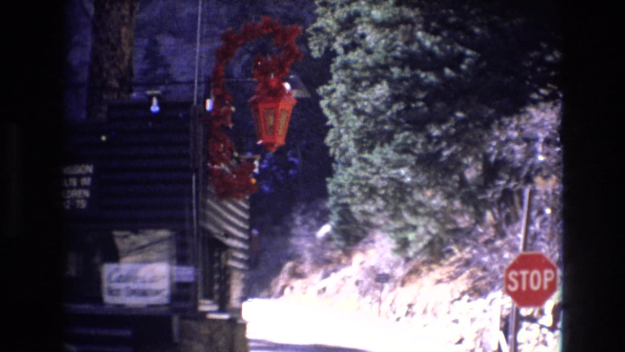 1973 Colorado 8mm frame showing a red stop sign, evergreen trees, rocky roadside terrain, and a partially visible holiday display near a rustic mountain setting.